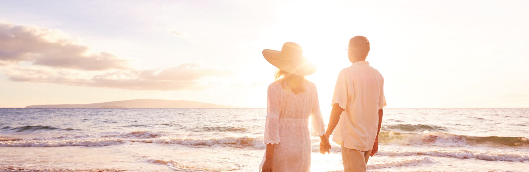 Couple walking across a beach against a sun